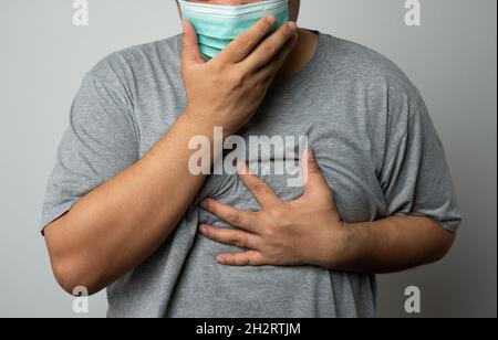 Kranker asiatischer Mann, der eine medizinische Gesichtsmaske trägt und hustet und seinen Mund mit meiner Hand bedeckt. Konzept zum Schutz des pandemischen Coronavirus und Atemschutzgeräts Stockfoto