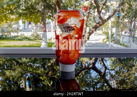 Leicht leere Ketchup-Flasche auf glänzendem Tisch und Holzschneidebrett. Stockfoto