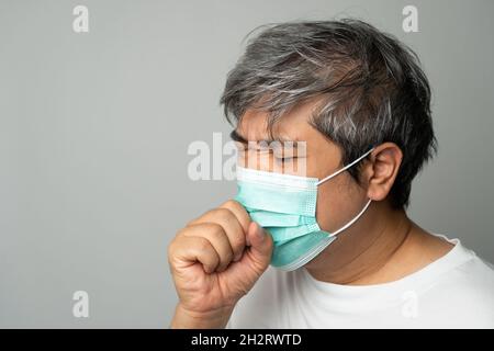 Kranker asiatischer Mann, der eine medizinische Gesichtsmaske trägt und hustet und seinen Mund mit meiner Hand bedeckt. Konzept zum Schutz des pandemischen Coronavirus und Atemschutzgeräts Stockfoto