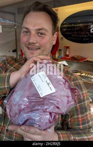 Neu Pudagla, Deutschland. Oktober 2021. Michael Fröhlich, Geschäftsführer der Firma Usedomer Wild, verkauft auf dem Gelände des Forstamtes in Neu Pudagla in der Gemeinde Ückeritz ein Bein Rotwildkalb mit Knochen aus seinem Verkaufswagen. Sein Unternehmen verkauft seine Produkte beispielsweise in den Märkten Rostock, Greifswald, Neubrandenburg und Anklam. Sie werden aus Wild aus der Region hergestellt - der Großteil davon wird von der Firma selbst auf der Insel Usedom gejagt. Quelle: Stefan Sauer/dpa/Alamy Live News Stockfoto