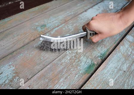 Ein Mann entfernt mit einem Drahtpinsel alte Farbe von der Holzoberfläche. Stockfoto