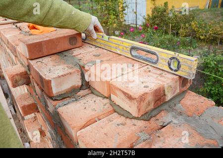 Mauerwerk, Mauerwerk. Nahaufnahme der Ziegelsteinlegung auf der Baustelle des Hauses. Der Maurer verwendet eine Geisterstufe, um die neue Ziegelwand im Freien zu überprüfen. Stockfoto