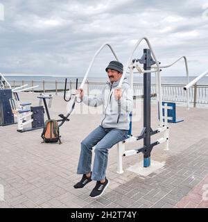 Ein älterer asiatischer Mann in legerer Kleidung arbeitet im öffentlichen Bereich am Wasser am Simulator. Stockfoto