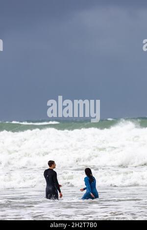 Schwimmer in Nassanzügen waten in Brandung am Strand von Polzeath in North Cornwall, Großbritannien Stockfoto