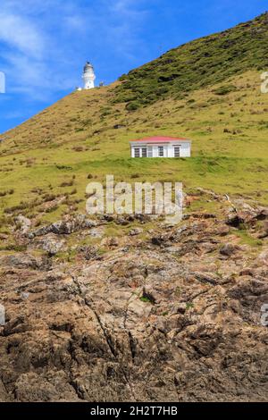 Kap Brett in der Bay of Islands, Neuseeland. Der historische Leuchtturm und eine Schutzhütte des Department of Conservation, darunter hoch aufragende Klippen Stockfoto