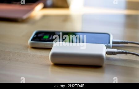 Ein Smartphone wird von einer kleinen weißen Powerbank geladen. Stockfoto