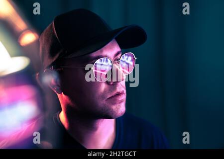 Futuristische Neontechnologie. Mann mit Brille in Zukunft Cyberpunk Beleuchtung. Lila fluoreszierende Farbe auf dem Gesicht. Studio-Porträt. Techno-Rave-Party. Stockfoto