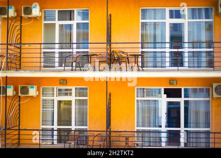 Geometrische Gebäudefassade mit großen Fenstern und Balkonen. Orangefarbener Putz. Stadtgeometrie. Freizeitmöbel auf dem Balkon. Stockfoto