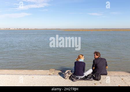 Pärchen sitzt bei Flut am Kai mit Blick auf die Baie de Somme und plaudert sich. Saint-Valery, Frankreich Stockfoto