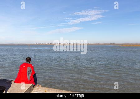 Mann in einem roten Mantel, der bei Flut die Baie de Somme betrachtet. Saint-Valery, Frankreich Stockfoto