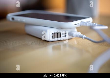 Ein Smartphone wird von einer kleinen weißen Powerbank geladen. Stockfoto
