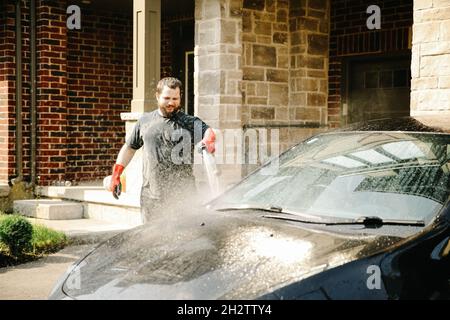 Mann, der das Auto mit Wasser und Jet vor dem Haus wascht. Stockfoto