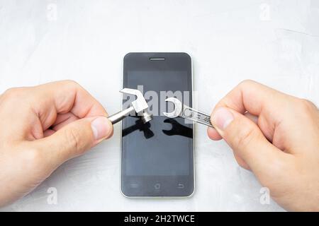 Hände, die kleine Handwerkzeuge über ein Smartphone auf einem Betontisch halten. Handy-Reparatur-Konzept. Stockfoto