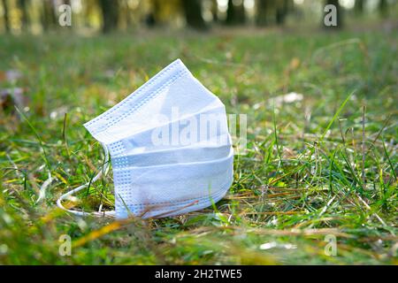 Gebrauchte chirurgische Gesichtsmaske, die auf dem Boden im Wald liegt. Umweltverschmutzung durch den umfangreichen Einsatz von Einwegmasken während der COVID-Pandemie. Stockfoto