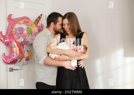 Portrait des Mannes umarmt Frau mit kleinen Baby-Tochter auf der Party mit Ballons im Hintergrund. Stockfoto