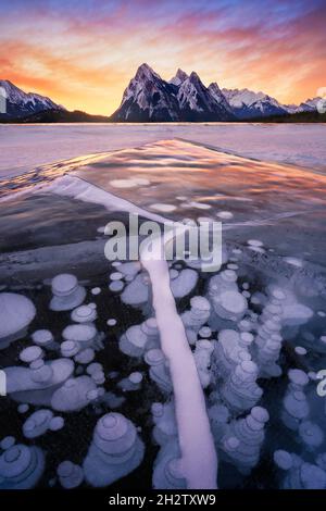 Atemberaubender Sonnenaufgang mit einer führenden Eiskröte und gefrorenen Methanblasen auf der Eisoberfläche, Lake Abraham, Alberta. Wintersturm in Kanada. Stockfoto