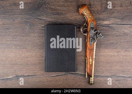 Draufsicht auf ein Buchcover und eine alte Pistole auf einem Holzhintergrund. Modell buchen. Speicherplatz kopieren. Stockfoto