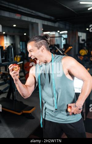 Junge gutaussehende Sportler hungrig und essen gesunde Apfelfrüchte im Fitnessstudio Stockfoto