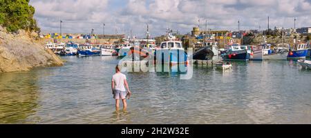 Ein Panoramabild eines Mannes, der im Meer am historischen, funktionierenden Newquay Harbour in Newquay in Cornwall steht. Stockfoto