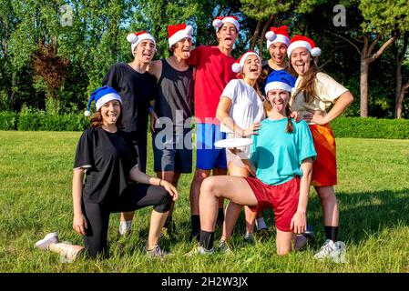 frohe weihnachten! Junge Gruppe von Teenagern Freunde Porträt feiert Weihnachten Zeit tragen weihnachtsmann Hut spielen Kunststoff-Disk-Spiel im Sommer im Freien Stockfoto