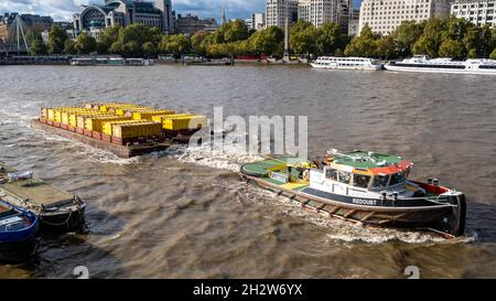 Arbeitsboot oder Schlepper, der einen Brage zieht, der Metallabfallbehälter entlang der Themse in London, England, transportiert Stockfoto