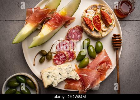 Schinken, Melonenscheiben, Brie- und Gorgonzola-Käse, Honig und Oliven auf grauem Hintergrund, Draufsicht Stockfoto