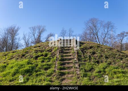Alte Hügeltreppe teilweise mit Erde und Gras bedeckt, vergessener Weg nach oben. Stockfoto