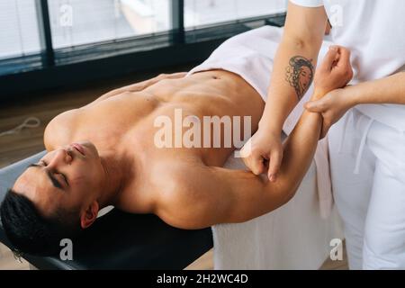 Nahaufnahme eines professionellen männlichen Masseurs mit starken Händen, der nach dem Sport-Training den Unterarm des muskulösen Sportlers massiert Stockfoto