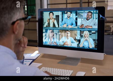 Geschäftsmann im Gespräch mit dem Team, das virtuelle Meetings am Computer leitet. Über der Schulter Stockfoto