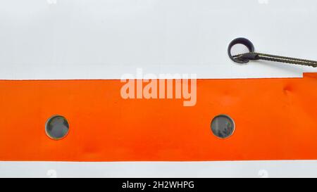 Nahaufnahme von zwei kleinen Bullaugen auf der weiß-orangen Seite des Schiffes Stockfoto