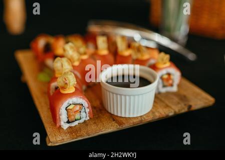 Sushi-Rolle mit Garnelenfleisch auf schwarzem Holzteller. japanisches Sushi-Essen. Maki und Brötchen mit Thunfisch, Lachs, Garnelen, Krabben und Avocado. Draufsicht Stockfoto