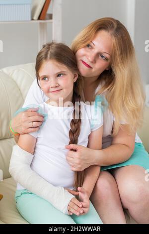 Mutter umarmt Ihr Mädchen mit einem Guss auf einem gebrochenen Handgelenk oder Arm lächelnd. Kinderkrankheiten, positive Aussichten und Genesung. Stockfoto