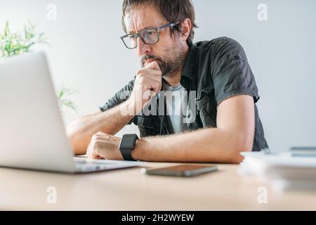 Freiberuflicher Mitarbeiter, der während einer Videokonferenz von der Inneneinrichtung des Heimbüros aus auf den Laptop-Bildschirm schaut, selektiver Fokus Stockfoto