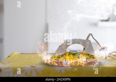 Jemand vergaß, das elektrische Bügeleisen zum Bügeln der Kleidung auszuschalten. Die Sohle des Eisens überhitzte, es entzündete sich und ein Hausbrand begann in der Stockfoto