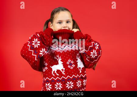 Portrait von fröhlichen Mädchen trägt roten Weihnachtspullover mit Rentieren, isoliert auf rotem Hintergrund Stockfoto