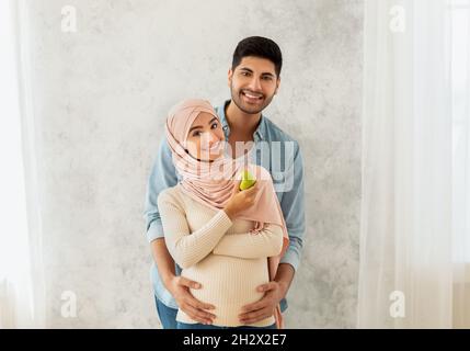 Gesunder Lebensstil während der Schwangerschaft. Liebende araber verheiratet Paar kuscheln, schwanger Frau aß Apfel Stockfoto