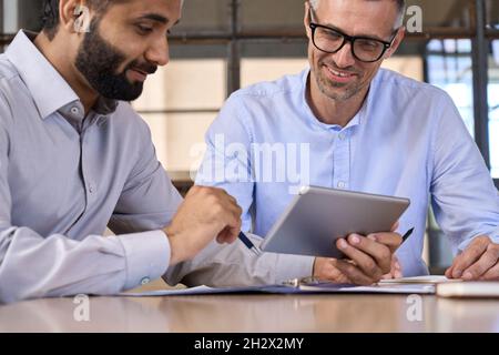 Zwei glückliche, vielfältige Geschäftsleute, die Finanzdaten mithilfe eines digitalen Tablets analysieren. Stockfoto