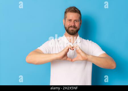 Junger hübscher Mann, der eine Herzfigur mit isolierten Händen auf blauem Hintergrund macht. Stockfoto