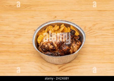 Gebratenes Huhn mit gerösteter Haut und Garnierung von hausgemachten Pommes in einem kreisförmigen Aluminium-Takeout-Behälter Stockfoto