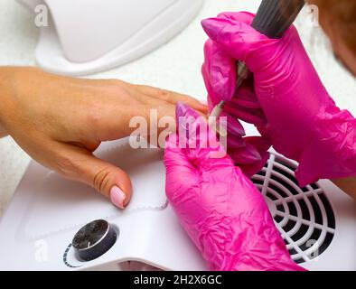 Ein Manikurist in rosa Handschuhen reinigt den Nagel vom Gellack des Kunden.entfernt Nagelhaut Hardware Maniküre. Professionelle Maniküre im Salon close-U Stockfoto