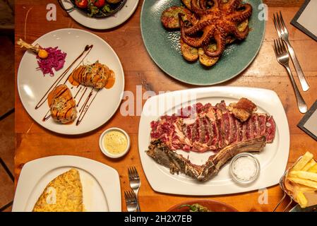 Set von großen Gerichten der spanischen Küche, gegrilltes Rindfleisch-Cutlet, Kabeljau Omelette, galicischen Oktopus mit Kartoffeln, Gabeln und Saucen Stockfoto