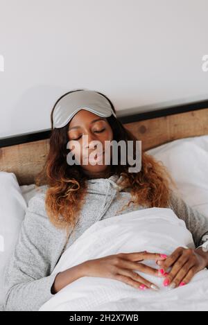 Eine schöne junge schwarze Frau, die auf dem Bett liegt und mit einer Schlafmaske schläft Stockfoto