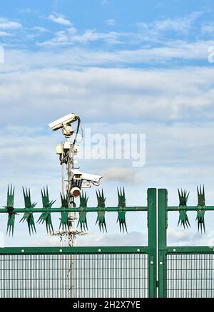Bank von Sicherheitskameras und Zaun mit rotierenden Spikes, die einen geschlossenen Standort in Großbritannien bewachen Stockfoto