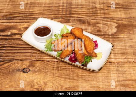 Knusprige Hähnchenstreifen, die mit Weizenmehl, Panko und Ei in Olivenöl mit Grillsauce überzogen sind Stockfoto