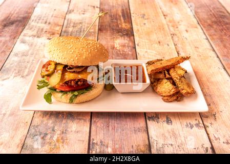 Veganer Erbsenburger mit Kartoffelkäse, eingelegten Pickles mit Tomaten und Pilzen mit Soße und gebackenen Kartoffeln Stockfoto