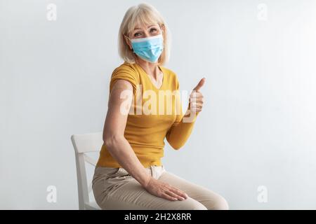 Geimpfte Senior Lady Gestikuliert Thumbs-Up Genehmigung Der Impfung Auf Grauem Hintergrund Stockfoto