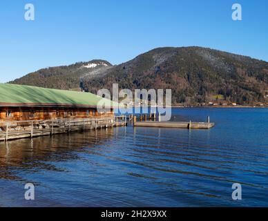 Eine schöne Aussicht auf den Tegernsee mit Bootshaus und Seebrücke in Bayern mit den winterlichen Alpen im Hintergrund an einem sonnigen Dezembertag (Deutschland) Stockfoto