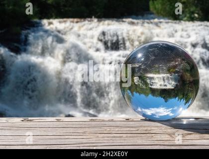 Eine Nahaufnahme einer Kristallschale mit einem breiten schäumenden Wasserfall im Hintergrund Stockfoto