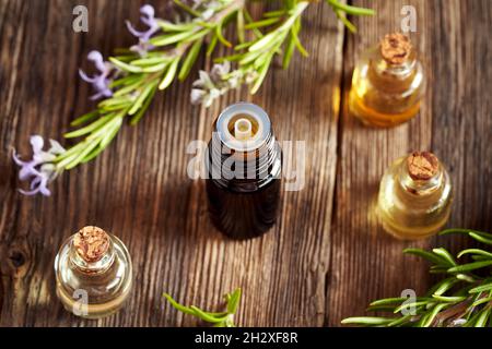 Eine dunkle Flasche ätherisches Öl mit frisch blühendem Rosmarin im Hintergrund Stockfoto