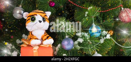 Weihnachten 2022 Neujahrstiger mit einem Geschenk in der Nähe des Baumes im Schnee. Schöner Kartenplatz für Text. Stockfoto